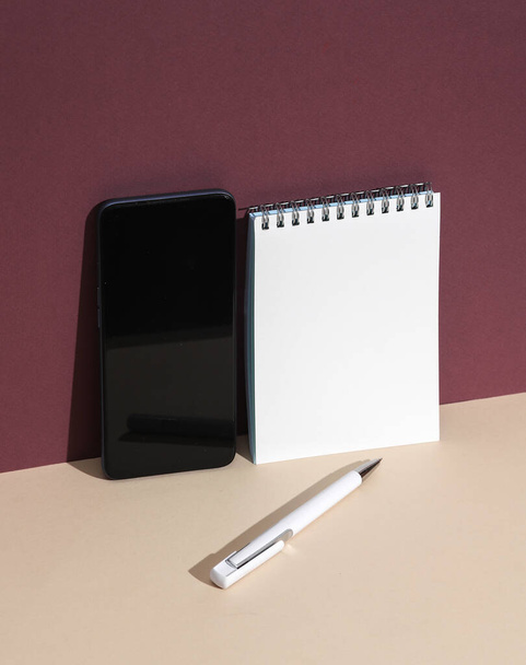 Smartphone, caderno branco com caneta em fundo bege Borgonha. Layout criativo - Foto, Imagem