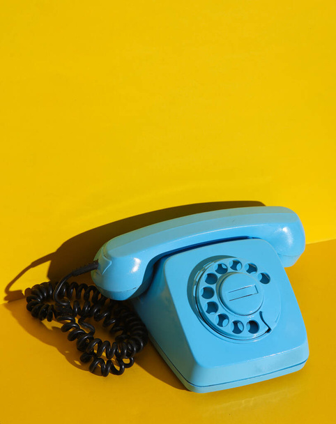 Obrotowy telefon obrotowy pomalowany niebieską farbą na żółtym tle ściany. Kreatywny układ - Zdjęcie, obraz