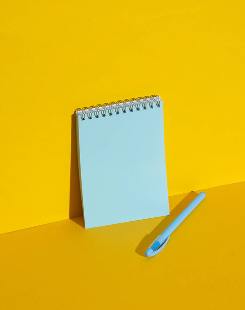 影のある黄色い背景のペンが付いている青いノート. クリエイティブレイアウト - 写真・画像