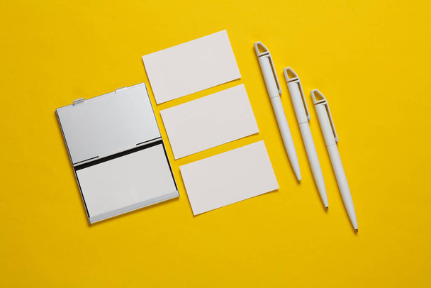 Держатель металлической коробки с визитками и ручками на желтом фоне - Фото, изображение