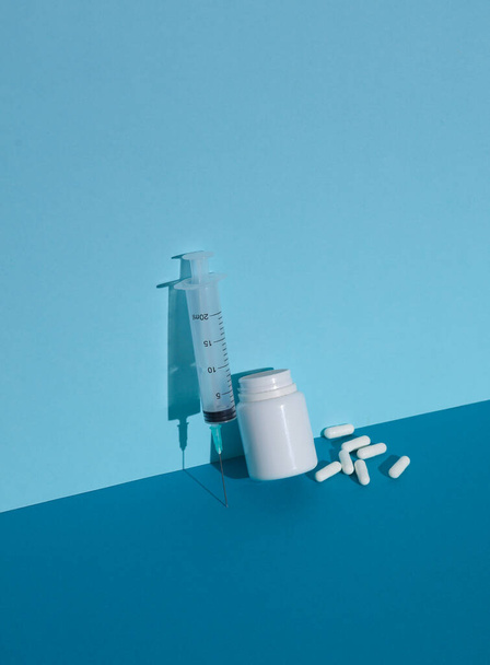 Flacone con pillole bianche e siringa su sfondo blu. Layout creativo - Foto, immagini