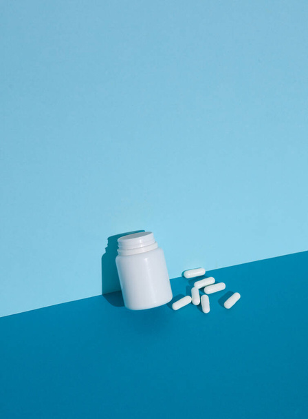 Flasche mit weißen Pillen auf blauem Hintergrund. Kreative Gestaltung - Foto, Bild