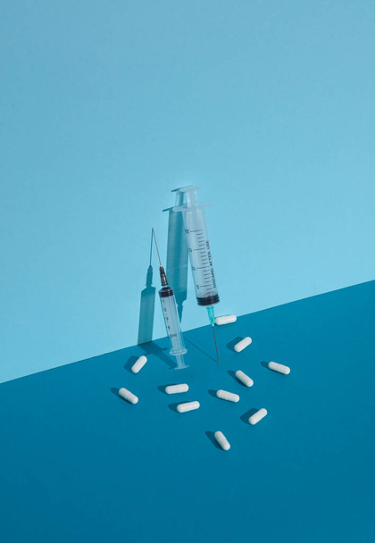 Spritze mit Pillen auf blauem Hintergrund mit Schatten. Kreative Gestaltung - Foto, Bild