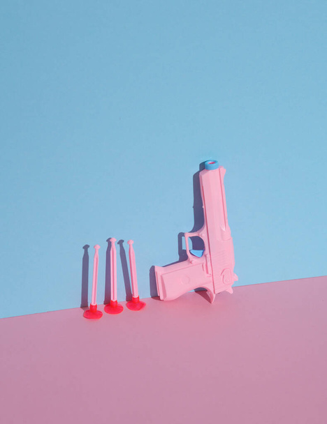 Spielzeugpistole aus Plastik auf blaurosa Pastellgrund. Minimalismus, kreatives Layout - Foto, Bild