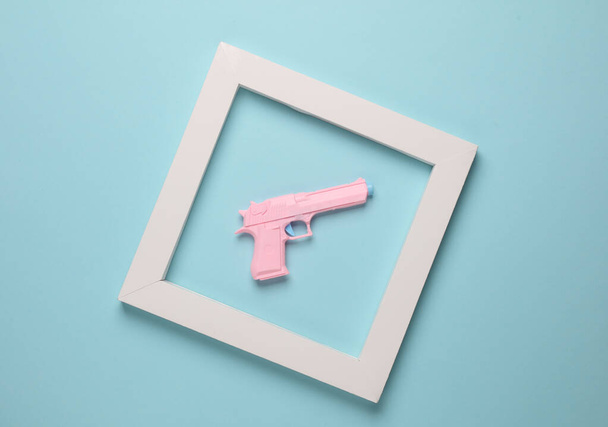 Plastic pistool in wit frame op een blauwe achtergrond. Minimalisme. Creatieve indeling - Foto, afbeelding
