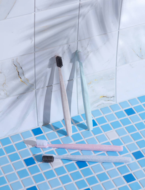 Plastic toothbrushes on tile with palm leaf shadow. Creative layout. Care and hygiene of oral cavity - Photo, Image