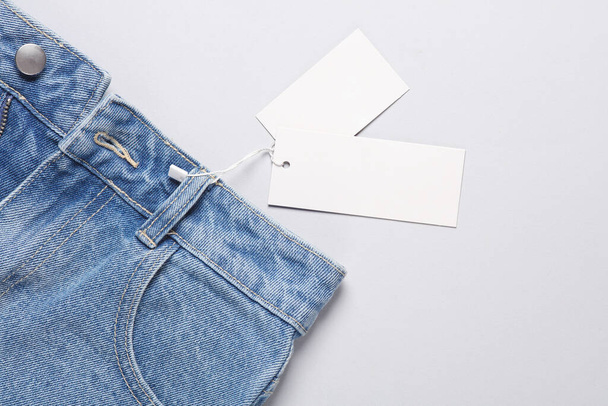 灰色の背景に白い価格のタグが付いている青いジーンズ - 写真・画像
