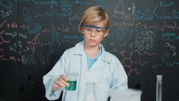 Chico inteligente inspeccionar líquido químico mixto en vasos de precipitados de laboratorio mientras sostiene y mira cuidadosamente. El niño caucásico se enfoca en hacer un experimento en la lección de química o en la clase de ciencias STEM. Erudición. - Imágenes, Vídeo