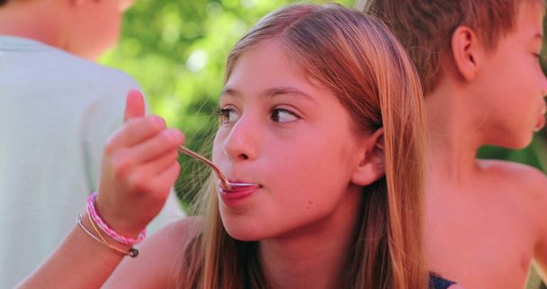 Upřímné děti spolu venku, holčička jí zákusek se lžičkou, dulce de leche - Fotografie, Obrázek