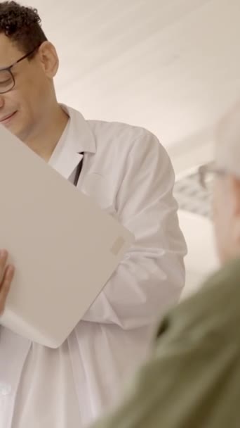 Βίντεο αργής κίνησης ενός γιατρού που γράφει δεδομένα σε ιατρική έκθεση και μιλάει με ηλικιωμένους - Πλάνα, βίντεο