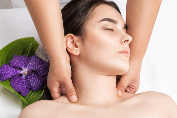 Masajista hace un masaje relajante en la cara, cuello, hombros y clavículas de una joven hermosa mujer en un spa. Cosmetología y concepto de masaje. - Foto, imagen
