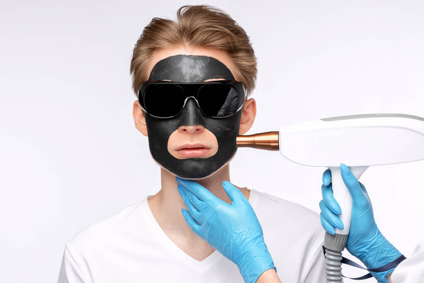 Beautician doet carbon peeling procedure om knappe man in schoonheidssalon. Hardware mannelijke cosmetologie. - Foto, afbeelding