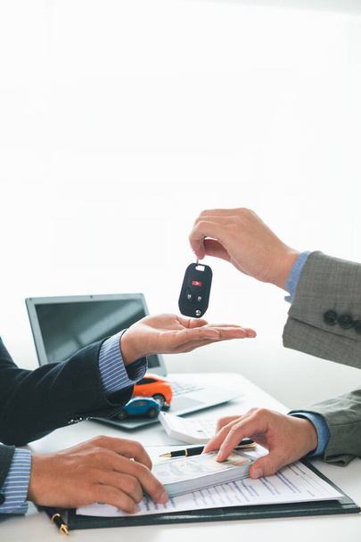 car dealer is handing over car keys to customer after sales contract and installment contract have been signed. Concept of handing over car keys to customers after the sales contract has been approved - Photo, Image