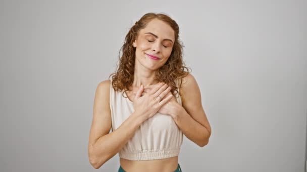 Confident young woman stands with hands on chest, eyes closed and a friendly smile, showing a sign of gratitude. white isolated, exuding beauty, health, and pride - a cheerful portrait! - Footage, Video