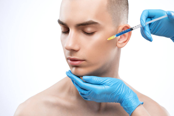 Mannen cosmetologie. Schoonheidsspecialiste maakt een man een verjonging injectie procedure op zijn gezicht. - Foto, afbeelding