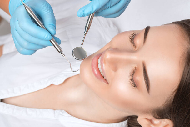Ένας οδοντίατρος θεραπεύει την τερηδόνα στο δόντι μιας νεαρής όμορφης γυναίκας σε οδοντιατρική κλινική. Γέμισμα δοντιών. - Φωτογραφία, εικόνα