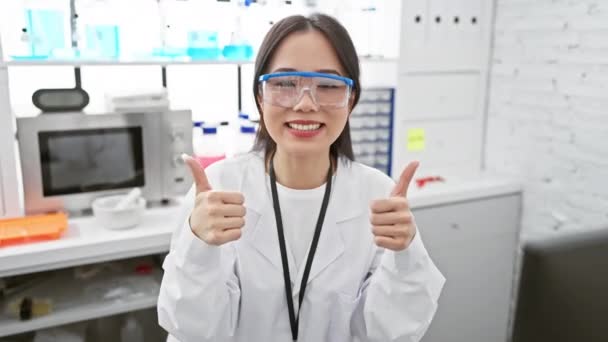 Alegre joven científica china, mostrando pulgares hacia arriba en un laboratorio, signo de éxito y positividad! irradiando felicidad mientras se regodea en su victoria. - Metraje, vídeo