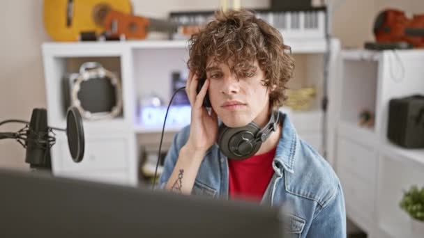 Άνδρας με σγουρά μαλλιά συγκεντρωμένος στο στούντιο μουσικής φορώντας ακουστικά και τζιν μπουφάν - Πλάνα, βίντεο