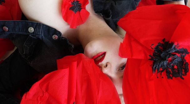 retrato de modelo de belleza seductora sensual rubia con labios rojos confeccionados y boca abierta sexy, con chaqueta vaquera negra acostada en grandes flores de amapola, espacio para copiar - Foto, imagen