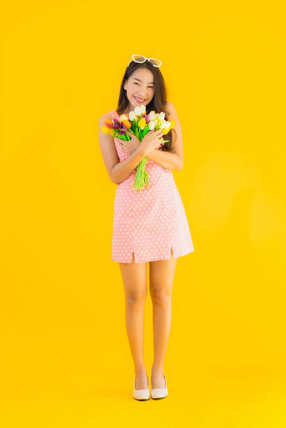Retrato hermosa joven asiática mujer con colorido flor en amarillo aislado fondo
 - Foto, imagen