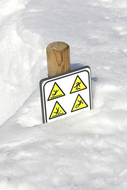 新鮮な雪は氷のために落ちて滑る危険を警告するピクトグラムとの警告の印を傷つけます - 写真・画像