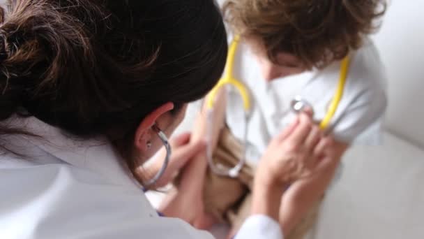 Vrouwelijke arts controleren hartslag van jongen patiënt met stethoscoop in kliniek - Video