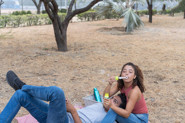 Pareja disfruta soplando burbujas juntos durante un picnic en el parque. - Foto, imagen