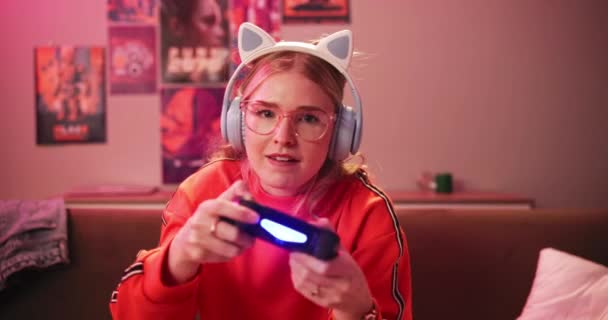 Headphones, face and woman playing video game in house for competition, rpg and online. Controller, girl and person on console technology for entertainment with neon light in portrait at apartment. - Footage, Video
