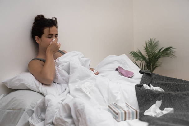 Egy beteg nő, zsebkendővel a kezében, orvosi cseppeket tart az ágyban, küzd a betegsége ellen..  - Fotó, kép