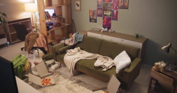 Špinavý, neuklizený a špinavý obývací pokoj v domě s odpadky a pizzou z rychlého občerstvení, nezdravý a vnitřní nábytek s oblečením. Byt, odpadky a nepořádek na pohovce nebo podlaze, chaos a zmatek - Záběry, video