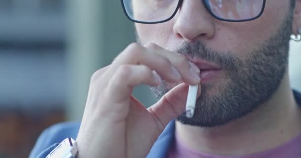 Zbliżenie młodego człowieka wdycha i wydycha dym papierosowy, pokazując szkodliwy wpływ tego niezdrowego trybu życia na jego układ oddechowy i ogólne samopoczucie. - Materiał filmowy, wideo