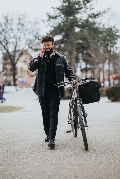 Ammattimainen mies liikekumppani osallistuu puhelinkeskusteluun kävellessään pyöränsä kanssa kaupunkiympäristössä.. - Valokuva, kuva