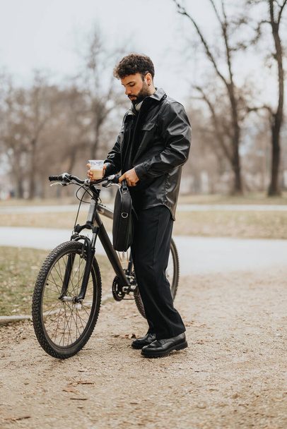 Елегантна чоловіча професійна багатозадачність з ноутбуком та кавою, спираючись на велосипед у міському парку. - Фото, зображення