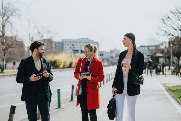 Jovens adultos em desgaste formal absorvidos em seus telefones enquanto caminham em uma cidade. - Foto, Imagem