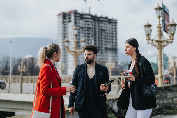 Un groupe de trois professionnels des affaires s'engage dans une discussion sérieuse à l'extérieur avec un arrière-plan de construction urbaine. - Photo, image