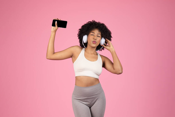 Mladý africký Američan žena v cvičení oblečení těší hudbu se sluchátky, ztělesňující radost a svobodu - Fotografie, Obrázek