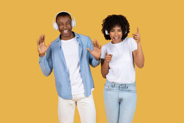 Жива афроамериканська пара з навушниками насолоджується музикою і показує грайливі танцювальні рухи - Фото, зображення