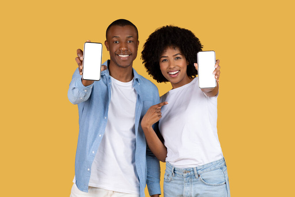 Афроамериканец мужчина и женщина, каждый держит смартфон с чистым экраном на желтом фоне - Фото, изображение