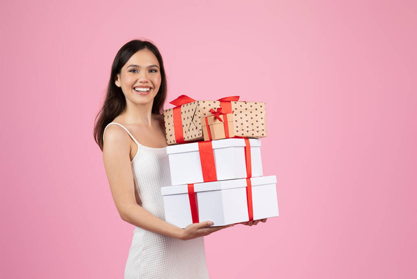 Radosna kobieta w białej sukience trzyma różne pudełka owinięte wstążkami, wyrażając szczęście i hojność - Zdjęcie, obraz