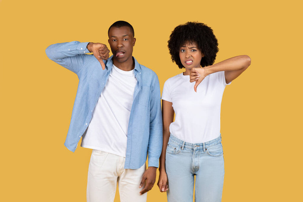 African American ζευγάρι κάνει αντίχειρες προς τα κάτω και time-out χειρονομίες που δείχνουν αποδοκιμασία και παύση σε ένα κίτρινο φόντο - Φωτογραφία, εικόνα
