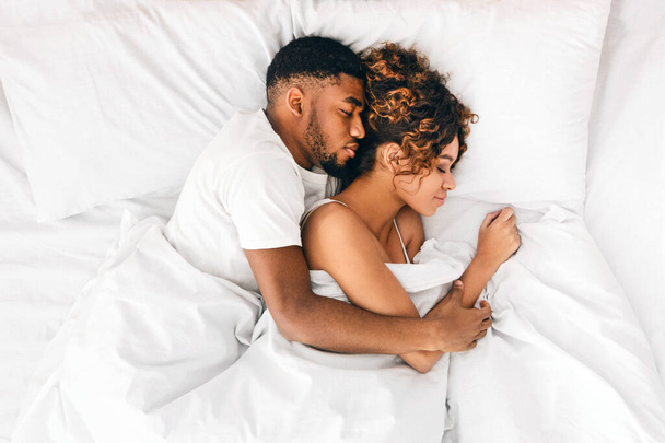 Szerető afro-amerikai házaspár alszik az ágyban, és átölelve, a szerelem és a gyengédség koncepció, felülnézet - Fotó, kép