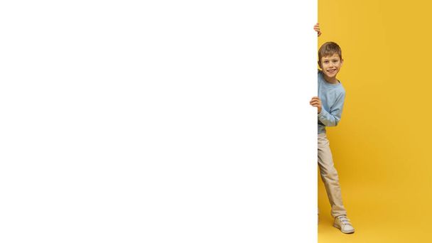 Νεαρό αγόρι παιχνιδιάρικα κρύβεται πίσω από ένα μεγάλο λευκό πανό με μόνο το πρόσωπο και το χέρι του δείχνει - Φωτογραφία, εικόνα