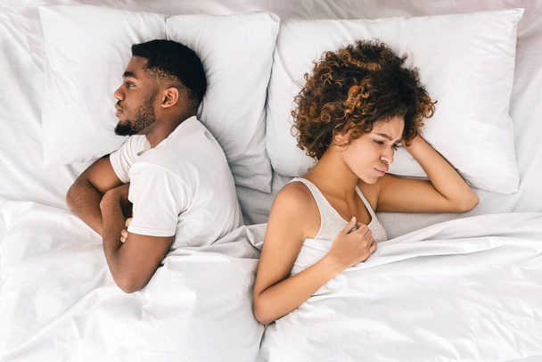 夫婦間の問題を持っている若い黒人カップルの動揺や意見の相違。背中合わせに横になっている、ベッドでお互いを無視して、トップ ビュー - 写真・画像