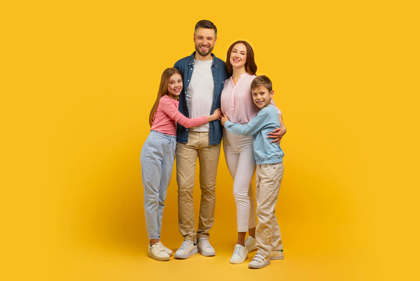 Щаслива сім'я з чотирьох стоїть близько разом з жовтим тлом, випромінюючи позитивізм, повну довжину - Фото, зображення