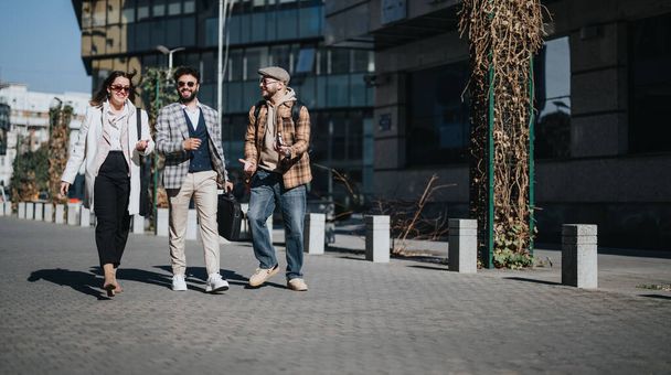 Трое молодых бизнесменов выходят на улицу, оживленно обсуждая рыночные стратегии и анализ проектов. - Фото, изображение