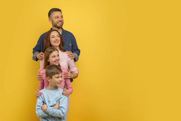 Famille de quatre personnes se tenant à proximité avec une expression heureuse et de contenu sur leurs visages, regardant l'espace de copie - Photo, image