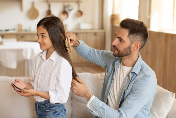 Padre attento spazzolando i capelli delle figlie, dimostrando cura e amore dei genitori nella vita di tutti i giorni - Foto, immagini