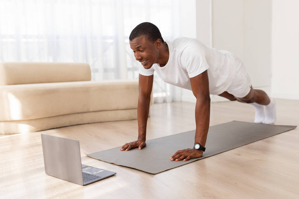 Esta imagem captura o homem afro-americano segurando uma posição push-up atentamente em um quarto arrumado e espaçoso - Foto, Imagem