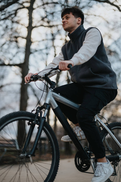 Un jeune adolescent homme au regard contemplatif en vélo dans un cadre paisible de parc au fur et à mesure que la journée s'estompe. - Photo, image