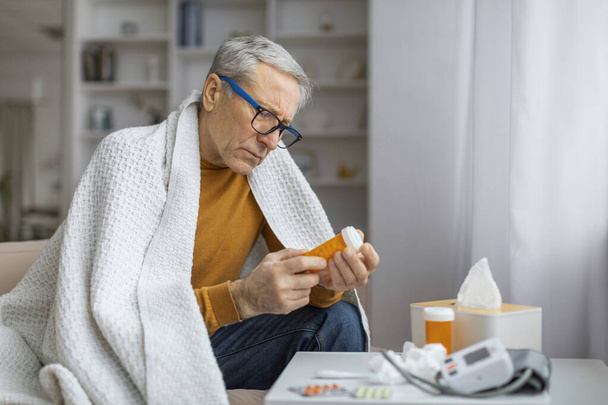 Homme âgé préoccupé tenant une bouteille de pilule, l'examinant de près, ce qui pourrait signifier une gestion de la santé ou une routine médicale - Photo, image